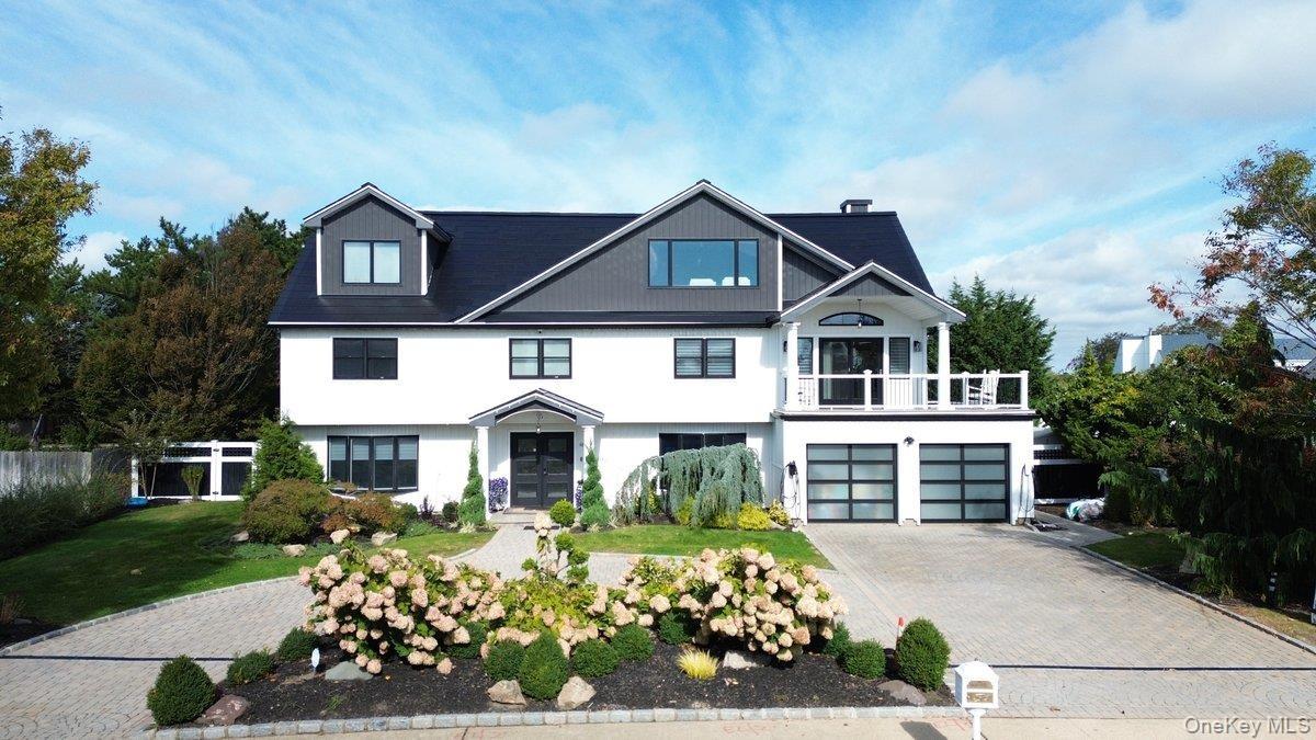 Two-story exterior featuring a high-contrast facade, dual glass-paneled garage doors, an elevated balcony, dormer windows, and a paver stone driveway
