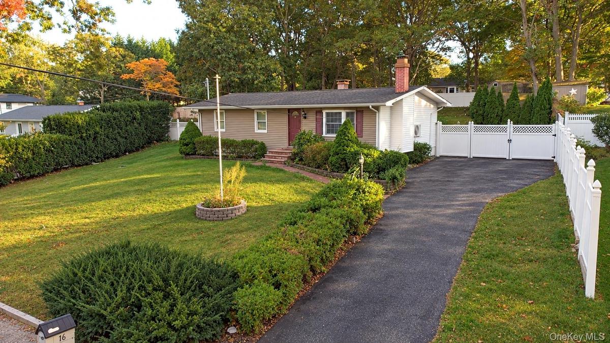 Ranch-style residence featuring a masonry exterior, asphalt driveway, vinyl fencing, chimney stack, and landscaped grounds