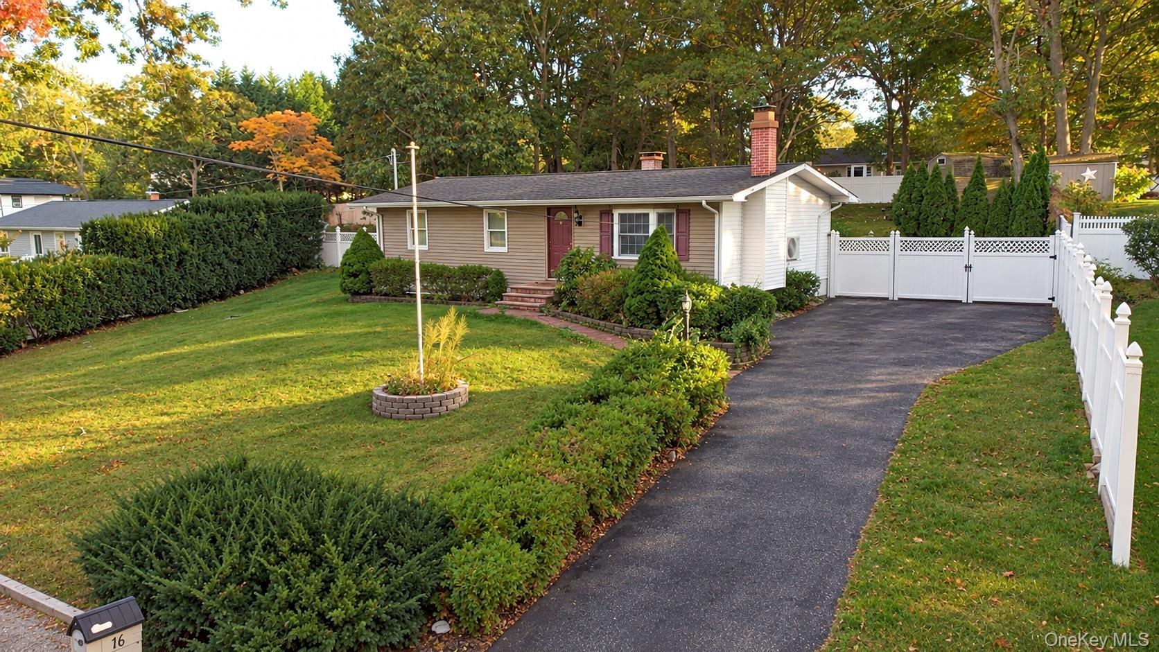 Ranch-style residence featuring a masonry exterior, asphalt driveway, vinyl fencing, chimney stack, and landscaped grounds