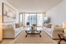 Living area featuring light-toned tile flooring, floor-to-ceiling glass paneling, and an expansive sliding door leading to an outdoor balcony