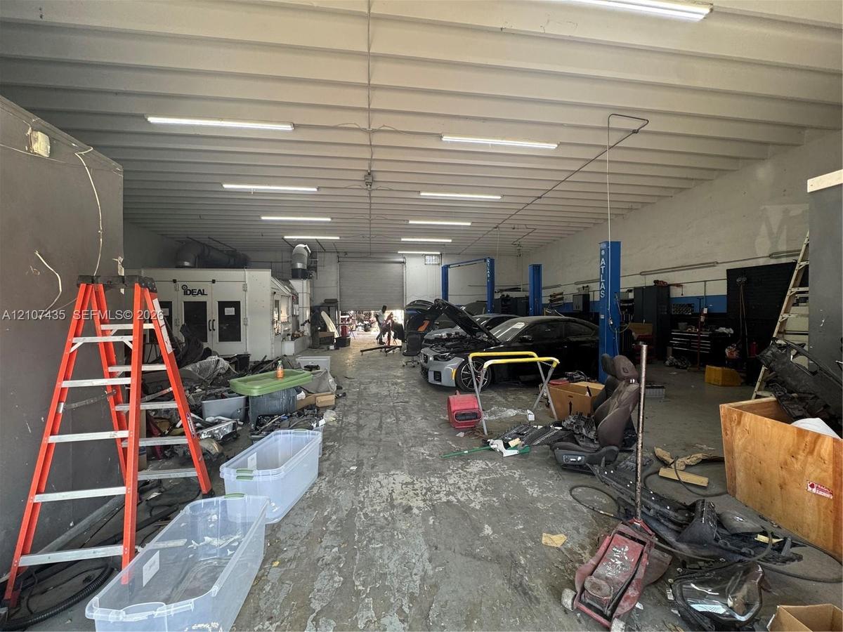 Open-span industrial workspace featuring high-clearance ceilings, industrial-grade fluorescent lighting, integrated automotive service lifts, and a pr