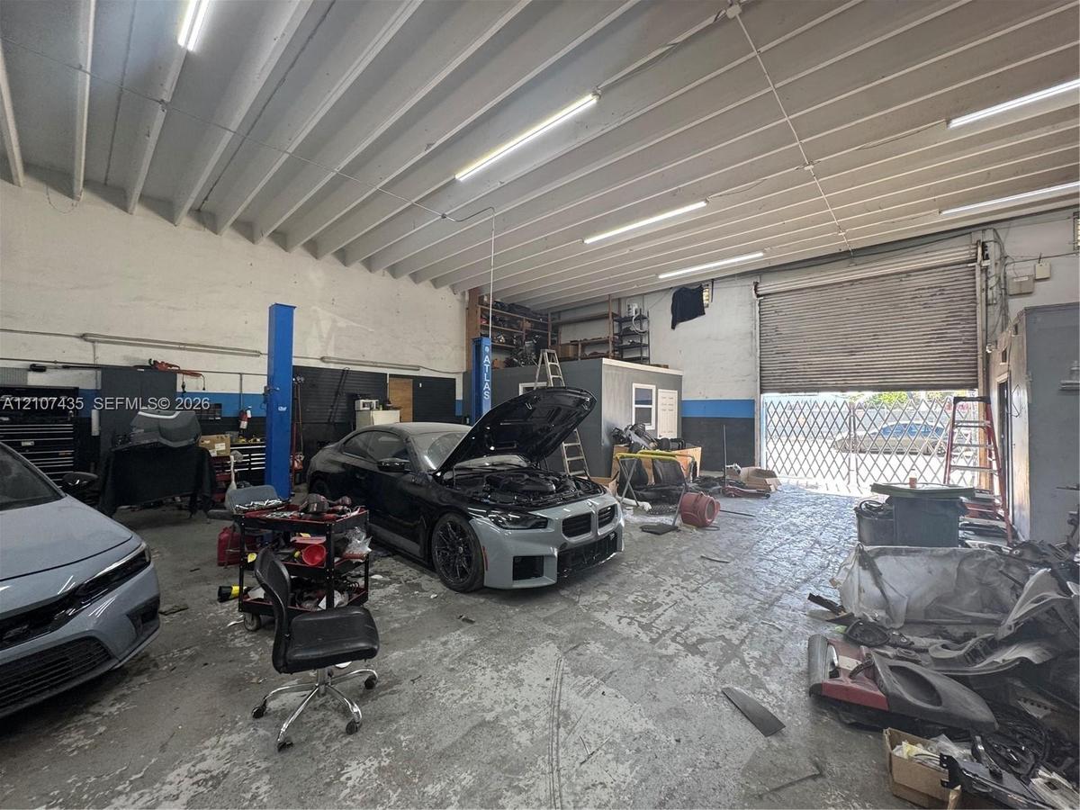 Spacious garage featuring a concrete floor, exposed vaulted ceiling with linear lighting, integrated hydraulic vehicle lift, and a roll-up bay door