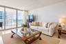 Floor-to-ceiling glass sliding doors, neutral stone flooring, and expansive exterior balcony. AI