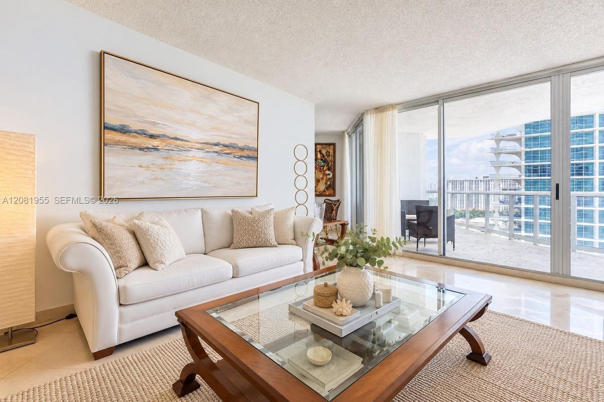 Living area featuring polished stone flooring and floor-to-ceiling glass sliding doors opening to a spacious balcony