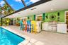 Screened lanai featuring a built-in outdoor kitchen with stainless steel grill, composite bar-height counter, recessed ceiling lighting, and pool with