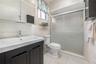 4th Bedroom En-Suite Bath. Dark wood-finish vanity with a rectangular sink, polished chrome faucet, tile-surround shower with frosted sliding glass do