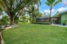 Expansive backyard featuring a manicured lawn, mature trees, and landscaped garden borders.