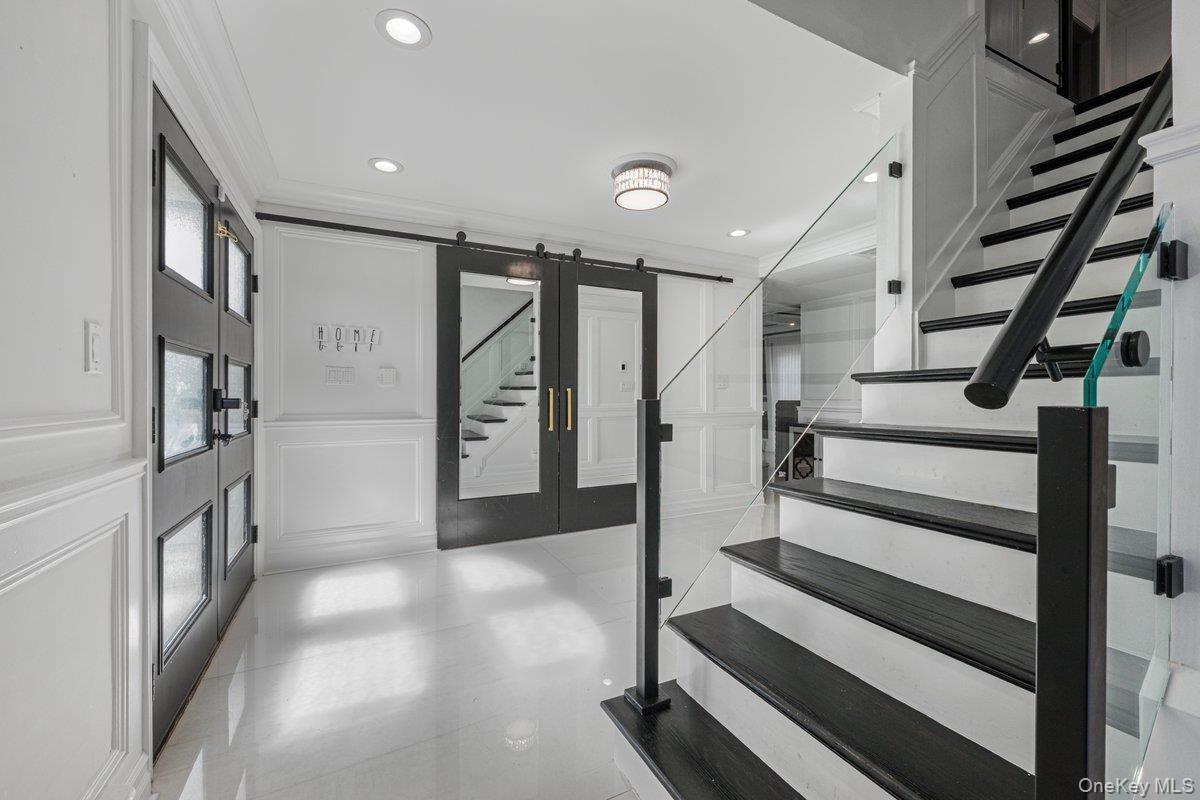 Foyer featuring high-gloss tile flooring, wainscoting, glass-panel entry door, sliding barn-style door with inset mirror, and staircase with glass rai