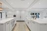 Kitchen featuring white custom cabinetry, dual islands with stone-look countertops, farmhouse-style sink, recessed lighting, and integrated panel-read