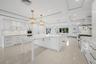 Kitchen featuring custom white cabinetry, dual oversized islands with stone-surface countertops, recessed coffered ceiling, polished tile flooring, an