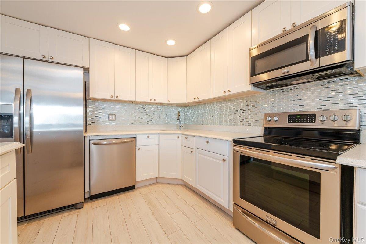 Kitchen featuring appliances with stainless steel finishes, a sink, light countertops, and white cabinetry