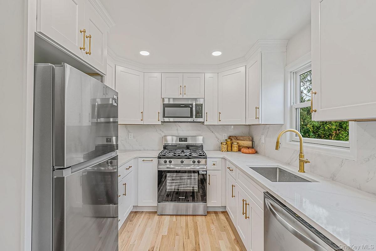 Kitchen featuring white shaker-style cabinetry, stainless steel appliances, light-toned quartz counters