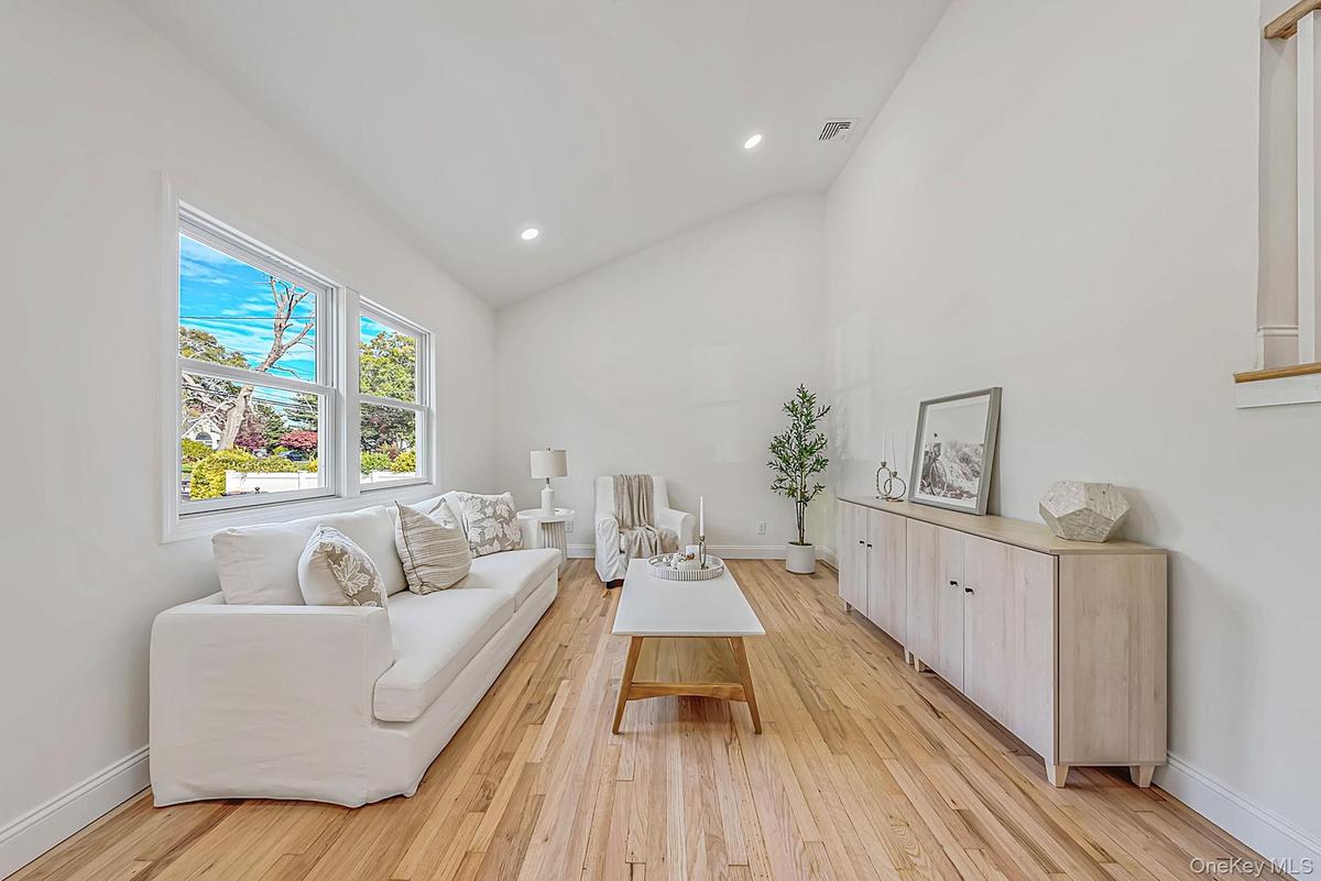 Living room with vaulted ceilings, wood-finish flooring, recessed lighting, and large windows