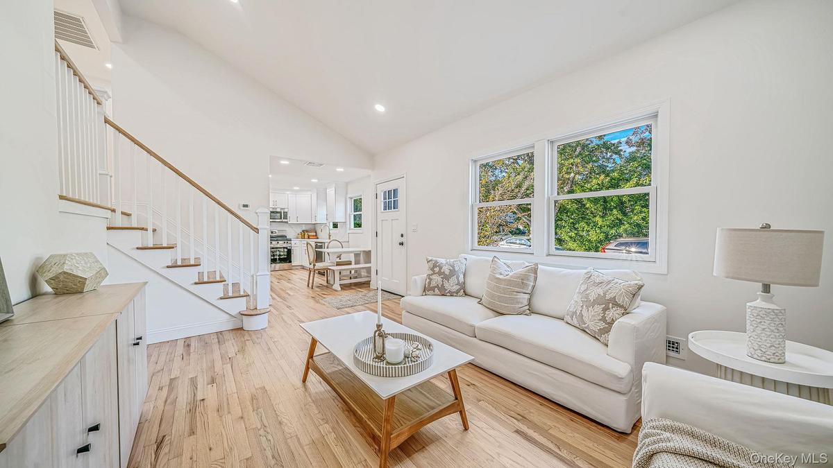 Living room with vaulted ceilings, wood-finish flooring, staircase with white railings, and large windows providing natural light