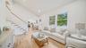 Living room with vaulted ceilings, wood-finish flooring, staircase with white railings, and large windows providing natural light