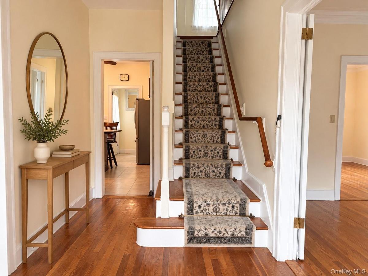 Foyer featuring hardwood flooring, a staircase with a wooden handrail, and patterned carpet runner