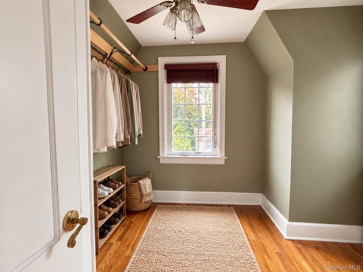 Custom wooden closet rod, wood-finish flooring, multi-pane window with white casing, and ceiling-mounted light fixture