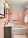 Bathroom featuring ceramic wall tiling with burgundy accent trim, a white porcelain pedestal sink with a brass-finish faucet, a brass-finish handheld 