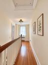 Hallway featuring wood-finish flooring, a decorative glass flush-mount light fixture, a wood-capped handrail with vertical balusters, and a multi-pane