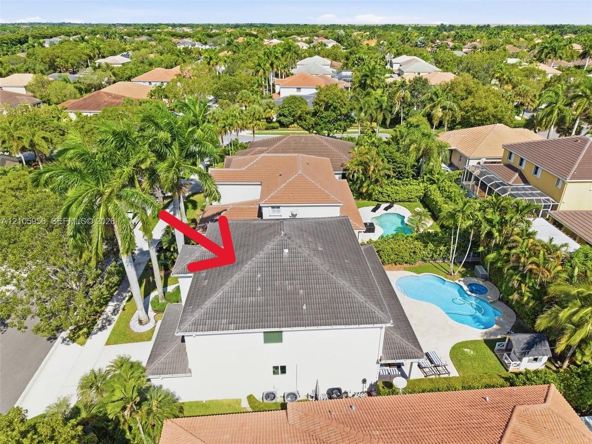 Aerial perspective of two-story residence featuring a tile roof, swimming pool with integrated spa, concrete pool deck, and mature palm trees