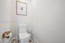 Minimalist powder room featuring a white dual-flush elongated toilet and a wall-mounted metallic gold finish toilet paper holder