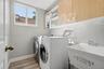 Laundry area featuring light wood-finish cabinetry, built-in shelving, a utility sink with a chrome faucet, and wood-finish flooring