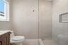 Wood-finish vanity, white countertop, walk-in shower with large-format wall tile, glass partition, and recessed shower niche