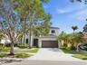 Two-story exterior featuring a light-colored stucco facade, tile roofing, an attached two-car garage, and established landscaping with mature trees an