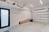 Finished garage featuring high-ceiling overhead storage shelving, linear LED lighting, and an exterior door with frosted glass paneling