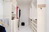 Walk-in closet featuring white built-in shelving, integrated dresser drawers, dual hanging rods, and large-format white tile flooring