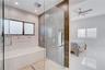 Walk-in glass-enclosed shower featuring a rainfall showerhead and wall-mounted sprayers, built-in soaking tub with textured wall tiling, and large-for