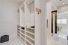 Walk-in closet featuring floor-to-ceiling custom white built-in shelving, hanging rods, and stone-finish tile flooring