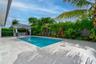 In-ground swimming pool with stone-tiled decking and a covered outdoor kitchen featuring built-in cabinetry and professional-grade appliances, enclose