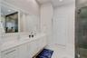 Double vanity with white cabinetry, light-toned stone-finish countertops, undermount sinks, large wall-spanning mirror, and a walk-in glass-enclosed s