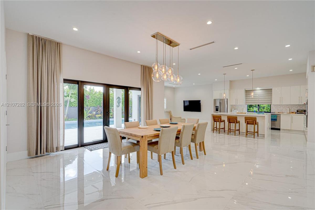 Open-concept interior featuring large-format polished stone flooring, recessed lighting, a modern multi-pendant chandelier, white slab-front cabinetry