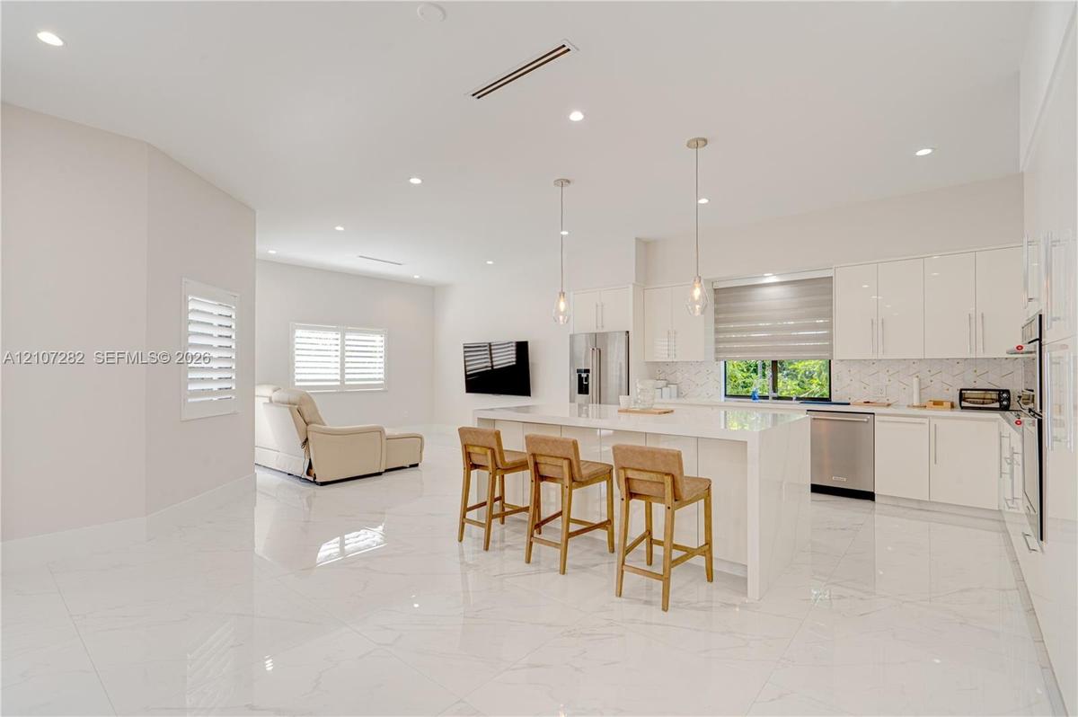 Kitchen featuring high-gloss cabinetry, stone-finish countertops, waterfall-edge island, polished tile flooring, and recessed lighting