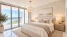 Floor-to-ceiling sliding glass doors, white tile flooring, drum pendant lighting, and a private balcony featuring a water backdrop ( AI used for inter