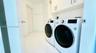 Laundry area featuring white large-format tile flooring, built-in upper cabinetry with brushed metal hardware, and a side-by-side front-loading washer