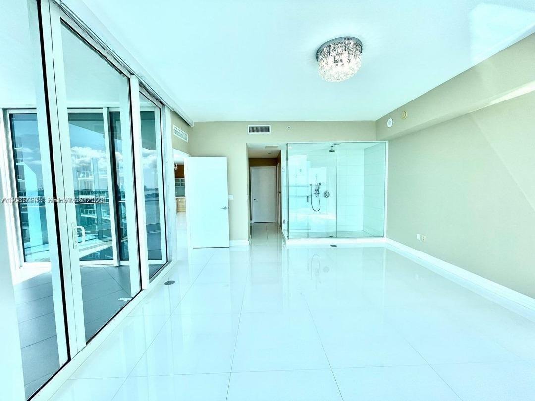 Polished tile flooring, floor-to-ceiling glass sliding doors, glass-enclosed shower, and decorative crystal flush-mount lighting