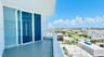 Covered balcony featuring large-format tile flooring and a glass-paneled railing, accessible through expansive floor-to-ceiling sliding glass doors