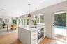 Kitchen island featuring a stone-look countertop, integrated cooktop, built-in oven, and white cabinetry, complemented by wood-finish flooring and pen