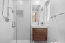 Bathroom featuring a wood-finish vanity with a rectangular sink, wall-mounted mirror, glass-enclosed shower with a built-in recessed niche, and polish