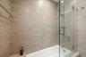 Full-height neutral-toned tile surround, frameless glass shower panel, chrome rainfall shower head with handheld attachment, built-in tub deck, and wa