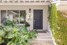 Entryway featuring a charcoal-painted front door, tiled steps, large picture window, wall-mounted metallic mailbox, and vine-covered stone siding