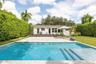 Outdoor area featuring a swimming pool with integrated steps, stone-finish pool deck, elevated wood-finish deck, and surrounding manicured privacy hed