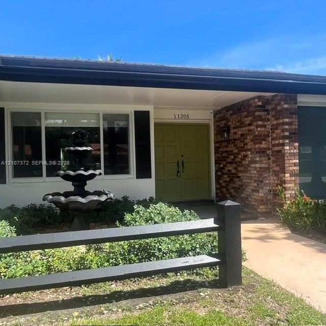 Exterior entry featuring double front doors, multi-tier decorative fountain, brick facade, and black post-and-rail fencing
