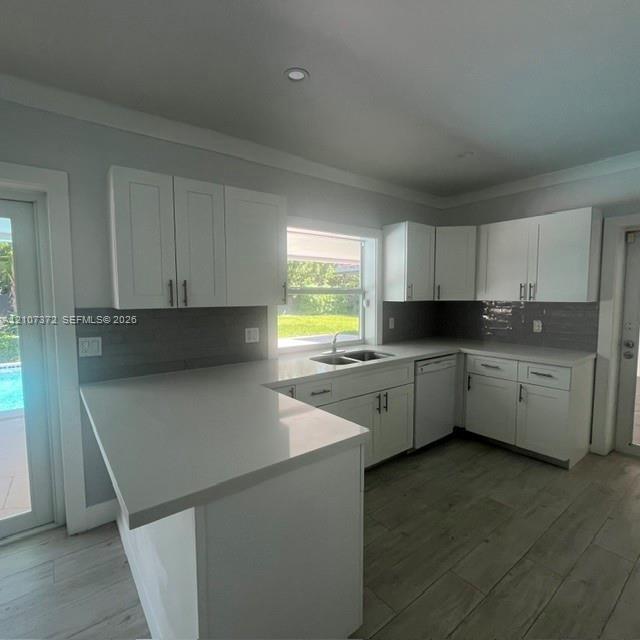 Kitchen featuring white shaker-style cabinetry, solid-surface countertops, grey subway tile backsplash, stainless steel dual-basin sink, and wood-fini
