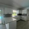 Kitchen featuring white shaker-style cabinetry, solid-surface countertops, grey subway tile backsplash, stainless steel dual-basin sink, and wood-fini