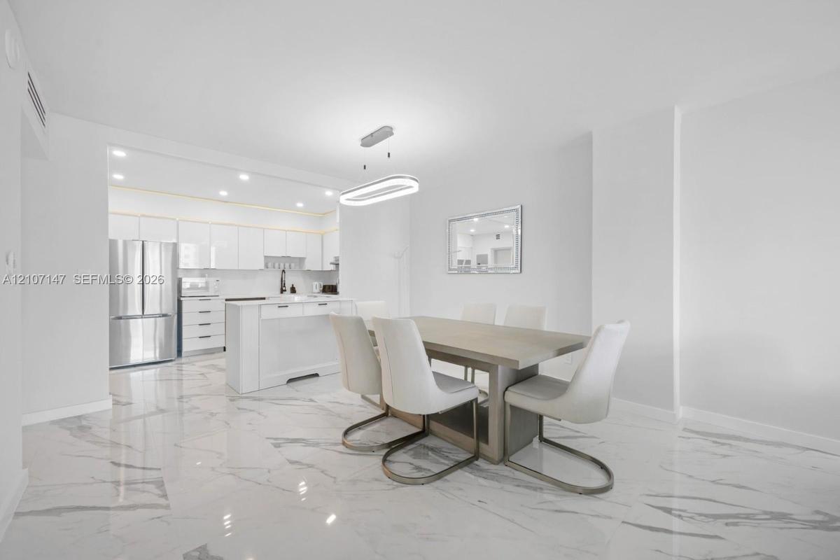 Polished stone-finish flooring, kitchen island with built-in cabinetry, stainless steel refrigerator, and modern oval-shaped pendant lighting