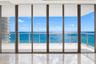 Floor-to-ceiling multi-panel sliding glass doors, private balcony with metal railing, and light-toned stone tile flooring